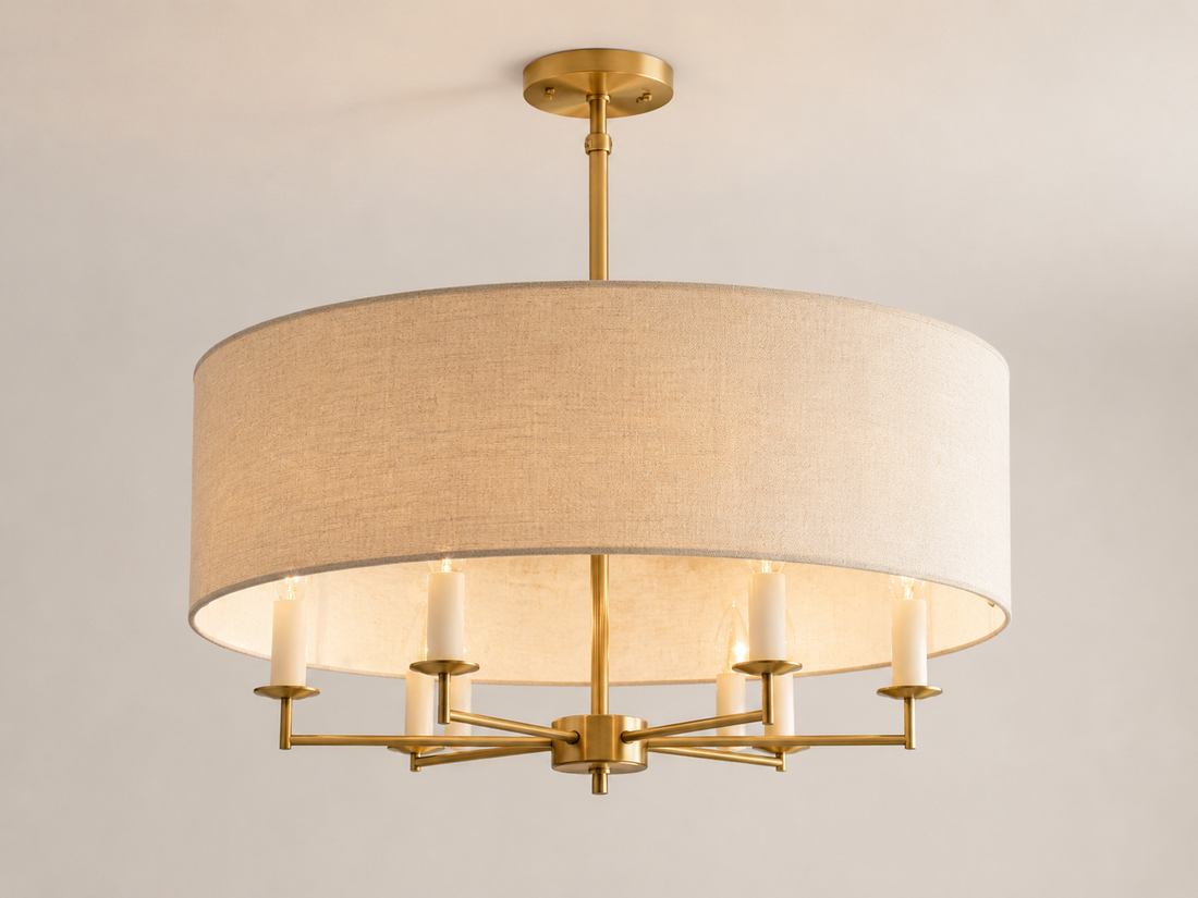 Linen drum chandelier with brushed brass frame hanging over a living room seating zone with sofa, armchairs, and coffee table