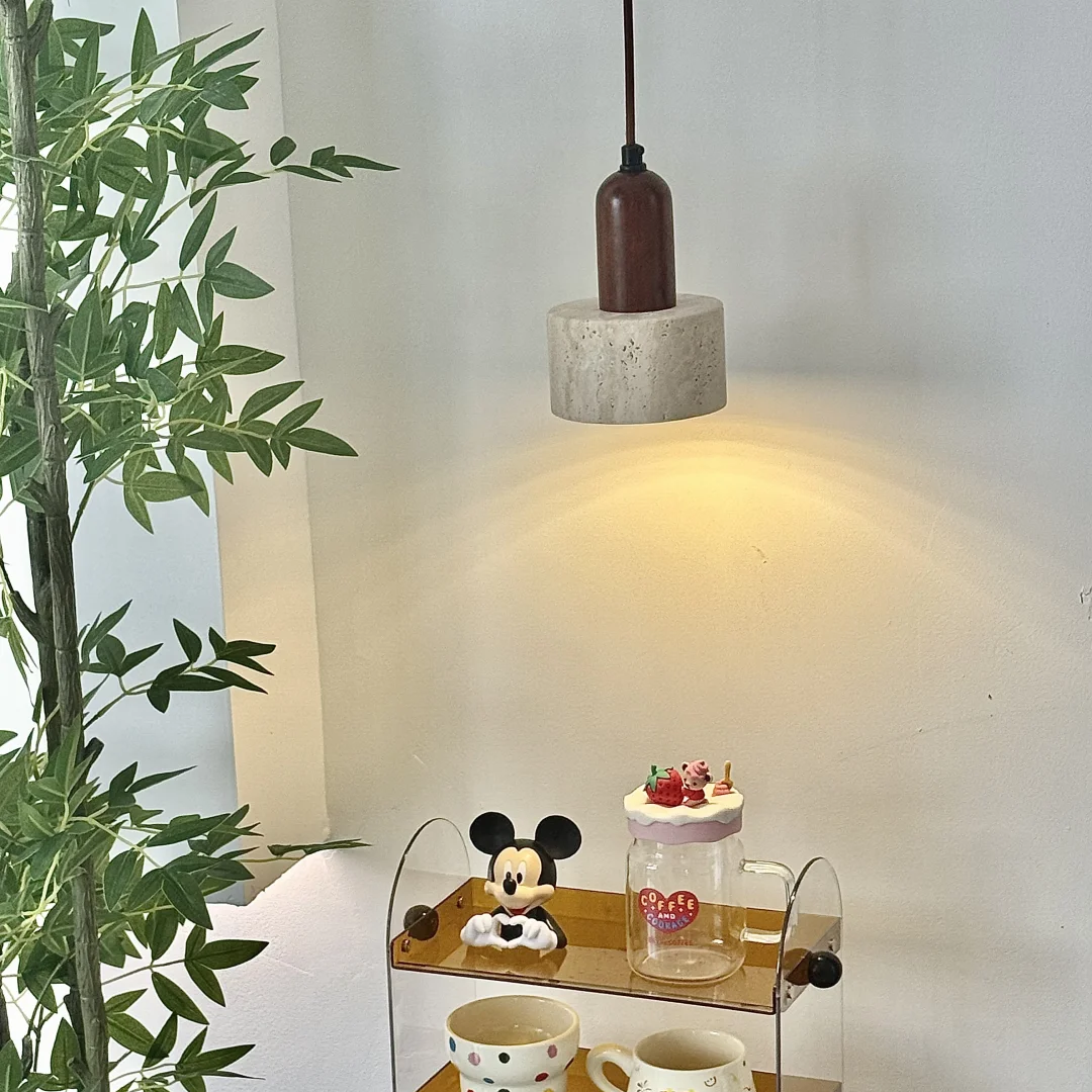 A three-tier acrylic coffee mug stand with wooden shelves, styled with various mugs, a Mickey Mouse figurine, and a small jar, set on a dark table next to a potted plant under a hanging light.