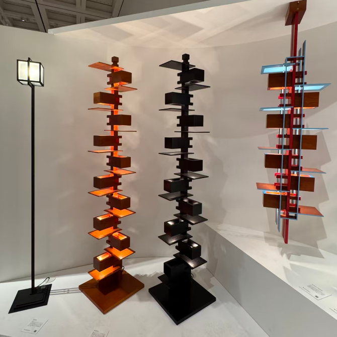 Three modern spiral shelving towers displayed in a minimalist gallery or showroom. The left tower is black with warm orange-brown wooden shelves and a black base.