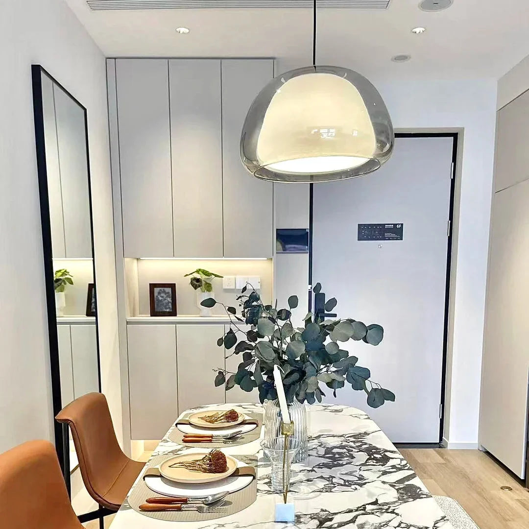 Curved glass pendant light with clear glass shade and warm lit glow, single hanging.