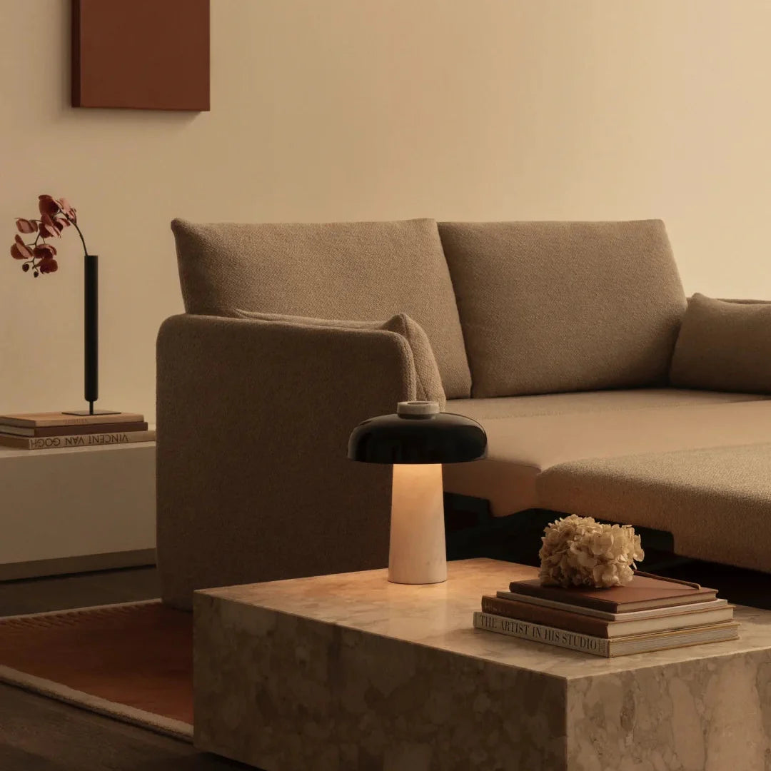 Table lamp with black dome shade and beige travertine base on a stone coffee table