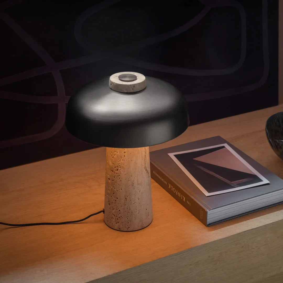 Mushroom table lamp on wood surface with black dome shade and beige travertine body