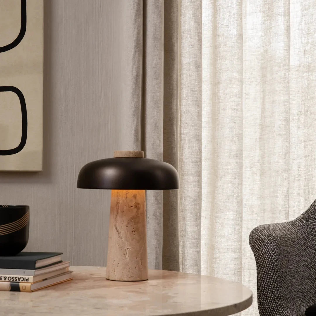 Small mushroom table lamp with dark dome shade and beige travertine pedestal base