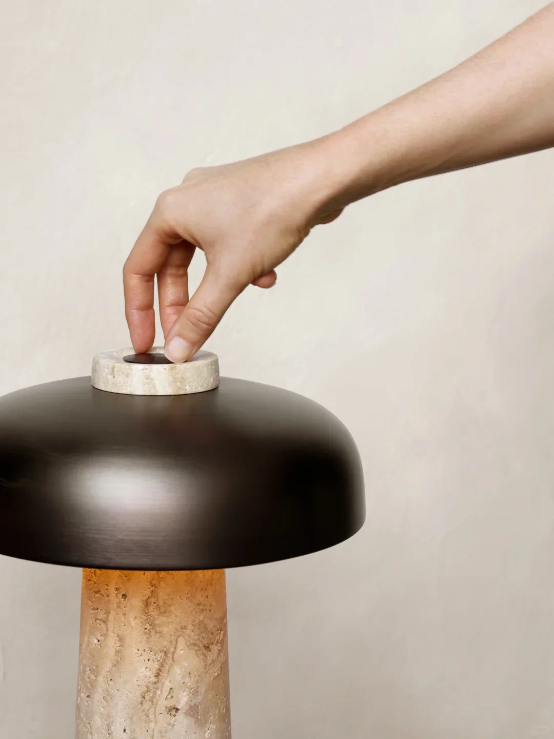 Hand adjusting the top of a mushroom table lamp; dark dome shade over beige travertine base