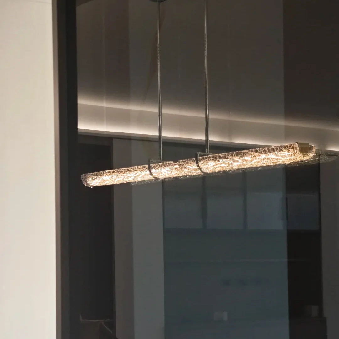 Close view of linear pendant light showing textured glass shade and metal hangers