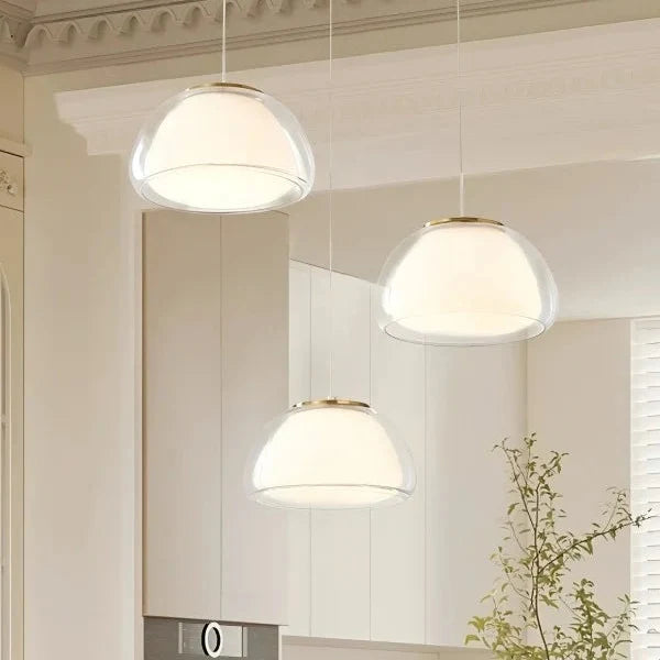 Curved glass pendant light set with clear domes and warm glowing interiors.