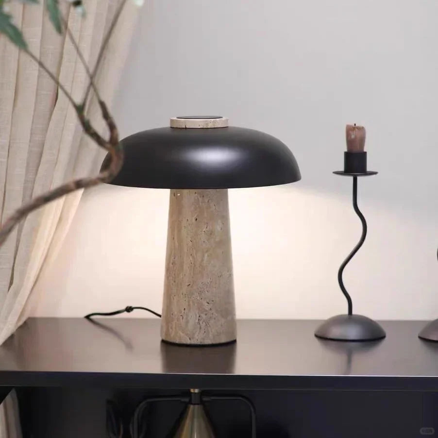 Travertine mushroom table lamp with dark dome shade and beige stone column base on side table