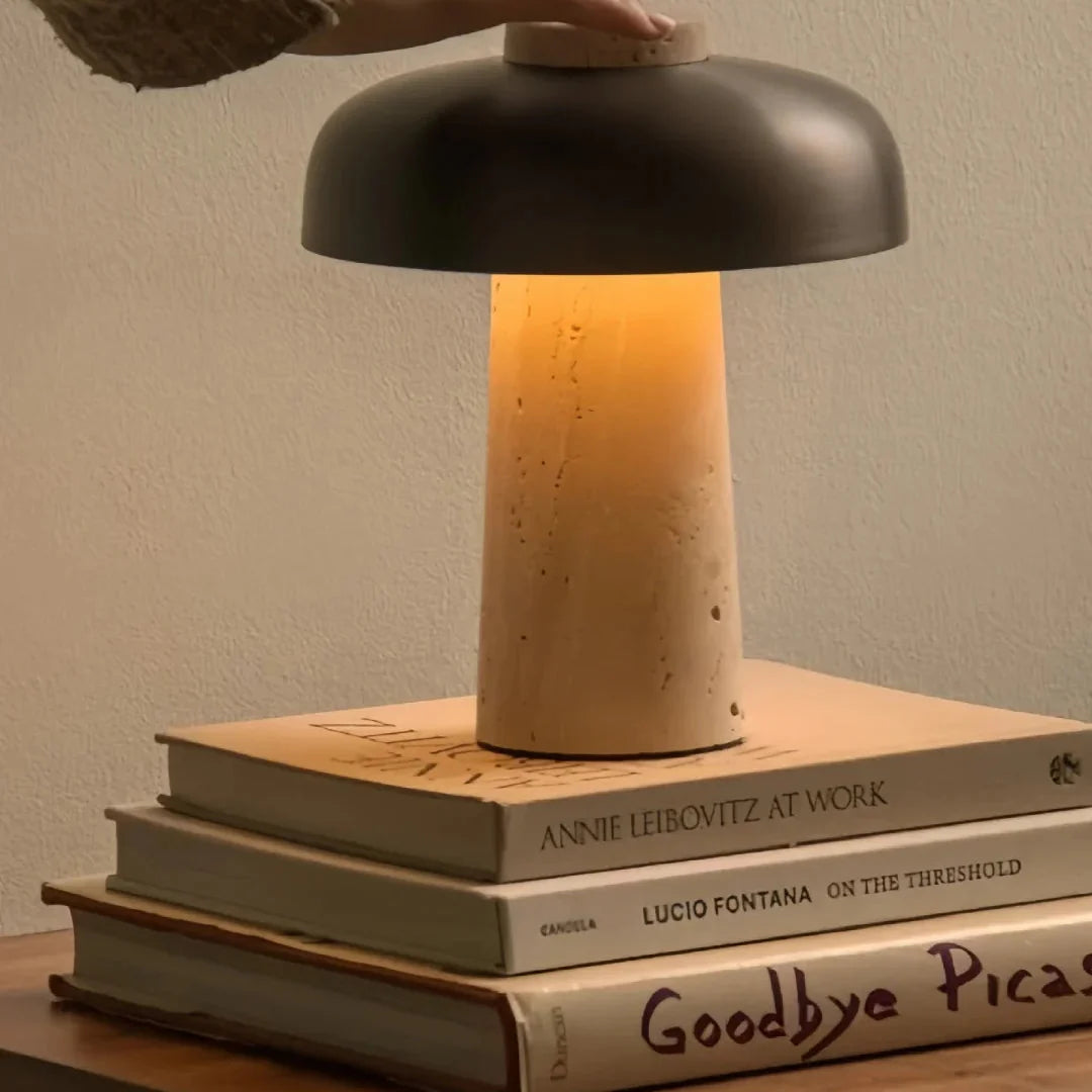 Mushroom table lamp showing warm glow through black dome over beige travertine column