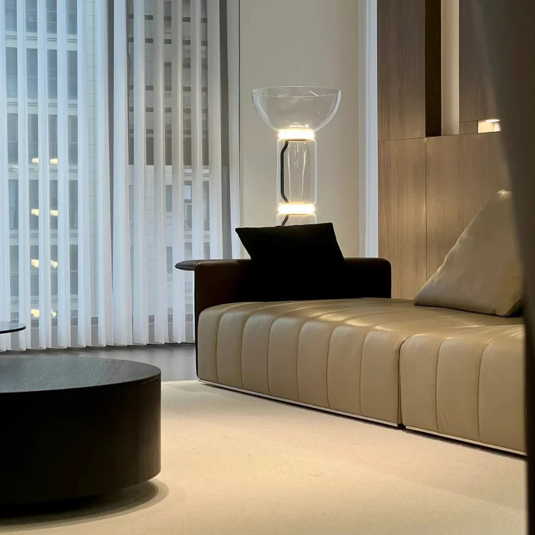 Glass floor lamp with lit clear bowl shade and glass column on black base.