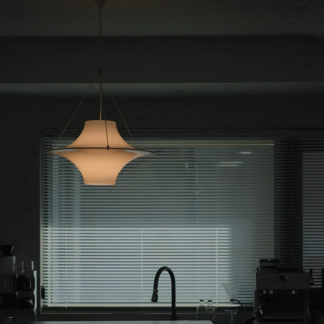 White disc pendant light with slender cords hanging above windows