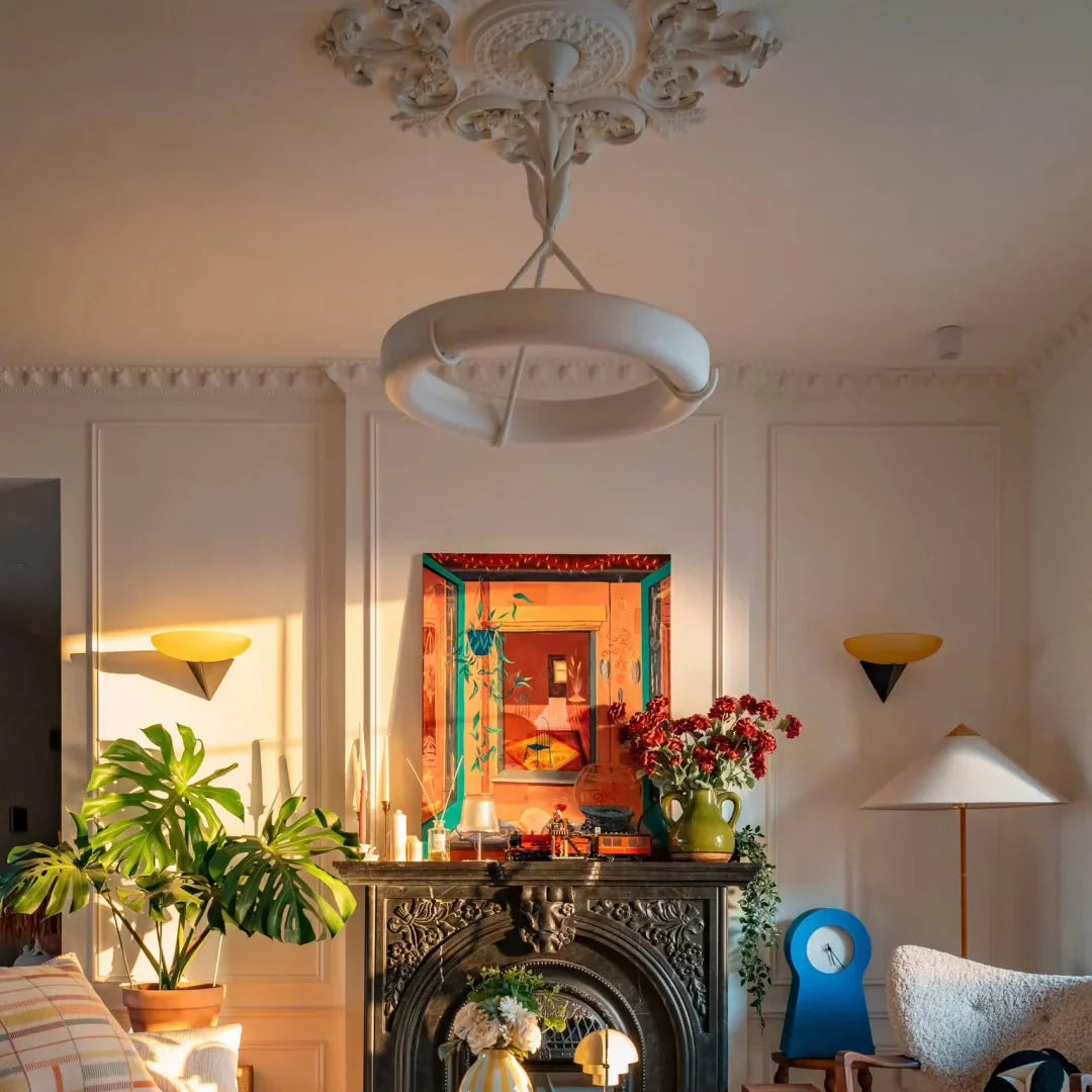 White sculptural chandelier with leaf stem and circular shade hanging above a fireplace mantel