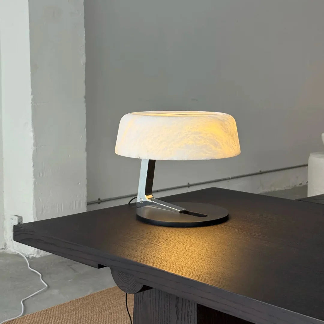 Alabaster table lamp with glowing opal shade and brushed metal base on dark tabletop