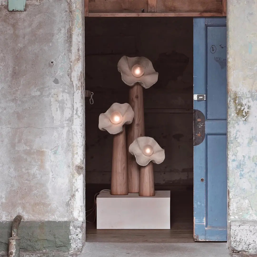 Three mushroom floor lamps on plinth, wood stems with textured shades and glowing bulbs
