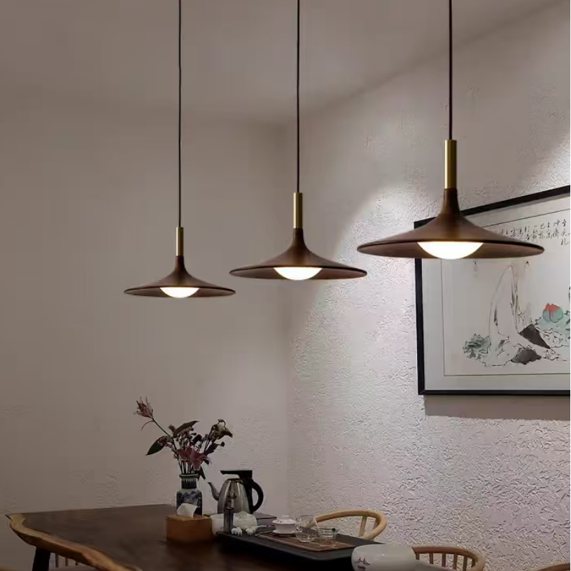 Three modern pendant light fixtures with bronze-colored metal shades and brass accents hang over a dining table in a styled interior room.