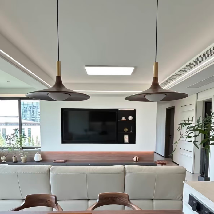A modern living room interior featuring two large pendant lights with dark bronze shades and brass accents hanging over a white leather sofa. A dark wood console table is positioned in front of the wall, with a television mounted above.