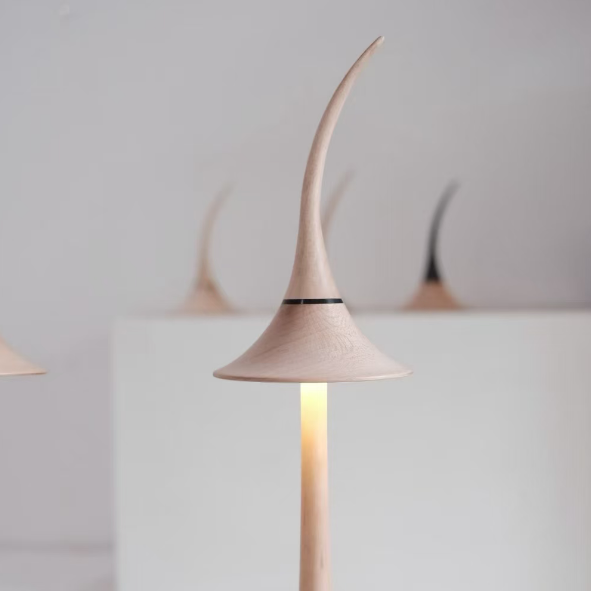 Close-up of maple wood cordless table lamp with curved shade and warm light glow.