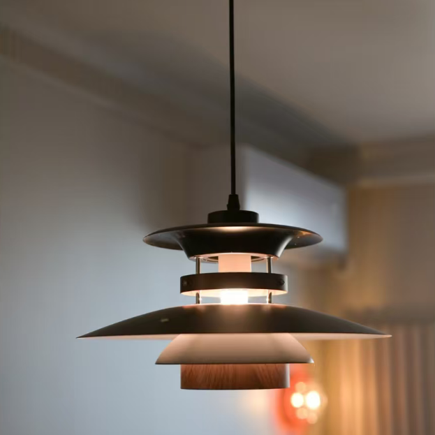 A modern multi-tiered pendant light with a black metal shade and a warm wood-grain middle tier, suspended by a black cord in an indoor setting.