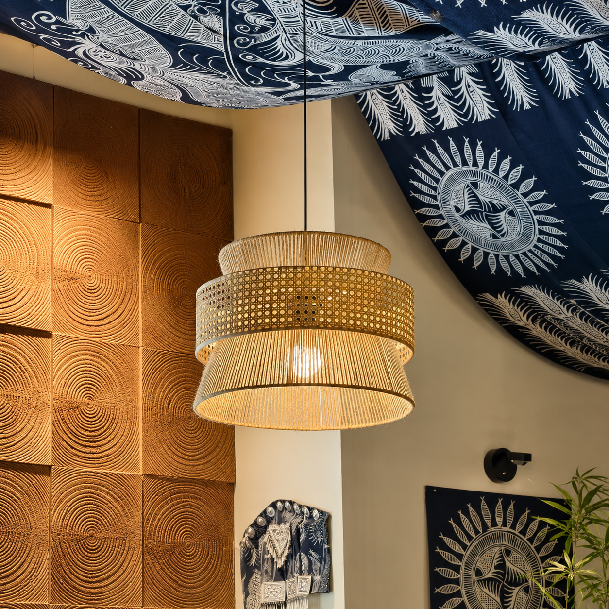 Woven hourglass pendant light with perforated drum shade hanging from black ceiling mount