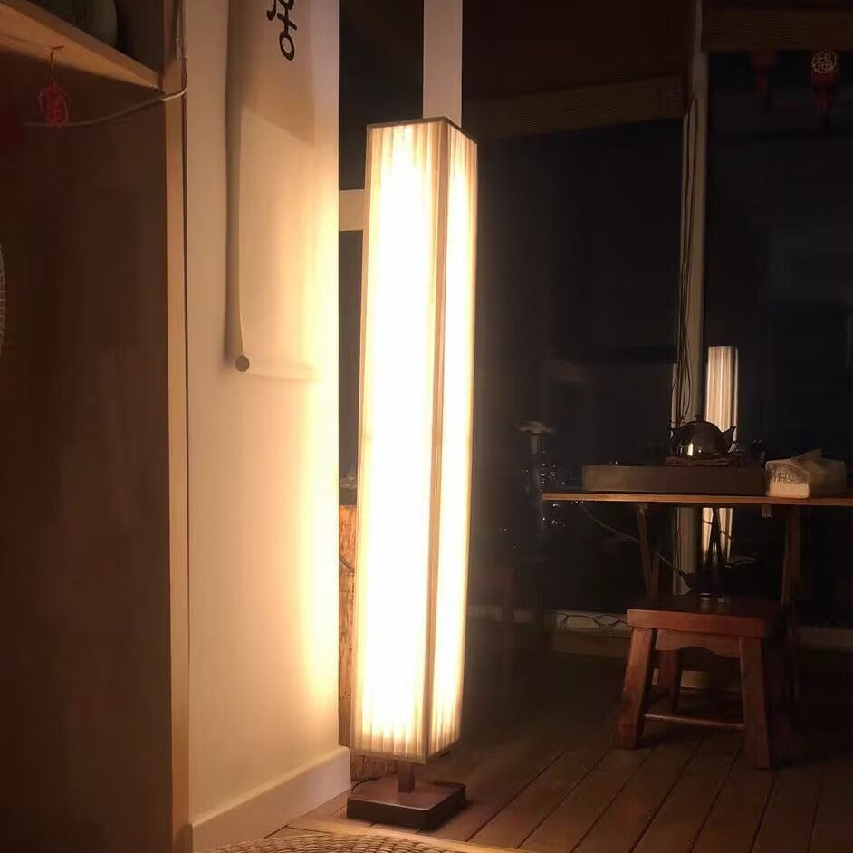 Slim tall floor lamp with off-white fabric shade and wood base, switched on