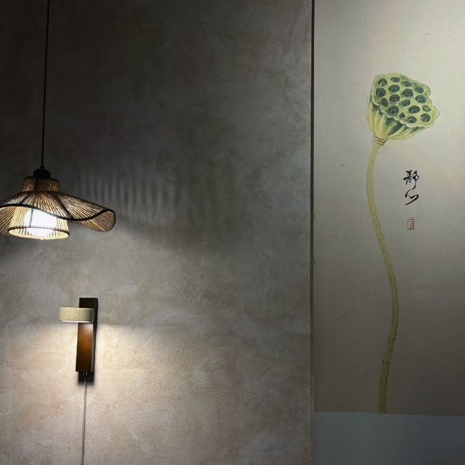 A modern wall-mounted sconce with a dark wood shade and warm light, shown mounted on a textured gray wall next to a vertical panel featuring a green lotus flower painting.