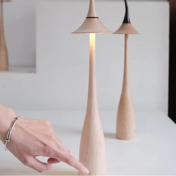 Cordless table lamp with maple wood body and curved shade, warm light on in a pair.