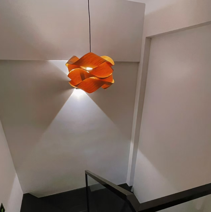 An orange flower-shaped pendant light hangs over a black staircase with a glass railing in a modern interior setting.