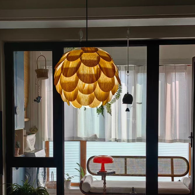 A large, textured pendant light with a golden-yellow, scalloped, lotus-like shade hangs in a modern living room setting, viewed through a black-framed glass door.