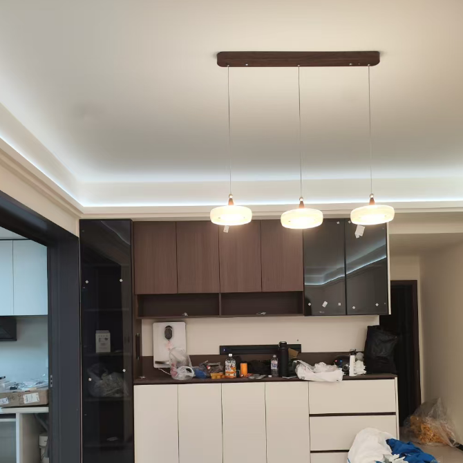 A modern kitchen cabinet set with dark brown wood upper cabinets, glossy black side cabinets, and white lower drawers, shown in a real interior space with pendant lights and floor clutter.