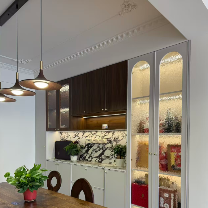 A modern kitchen and dining area featuring a tall white glass-front storage cabinet with warm interior lighting, next to a wooden dining table and chairs.