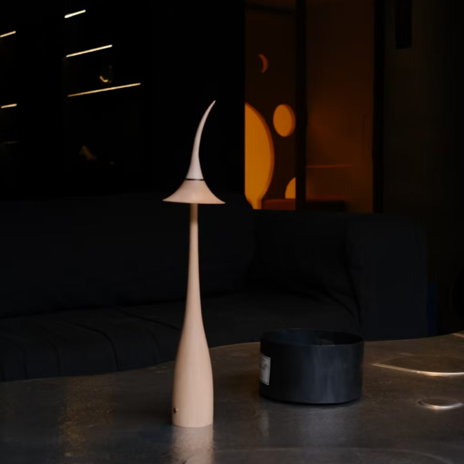 Glowing maple wood cordless table lamp with curved shade, set on a dark table.