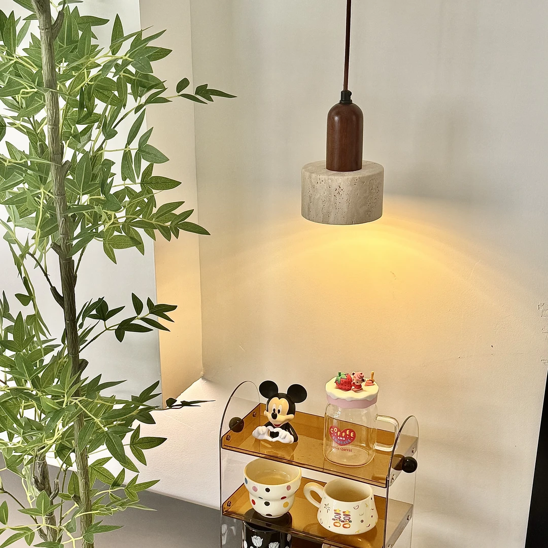 A two-tier acrylic and wood serving tray holding several colorful mugs and small decorative items, styled on a dark table next to a potted plant under a hanging pendant lamp.