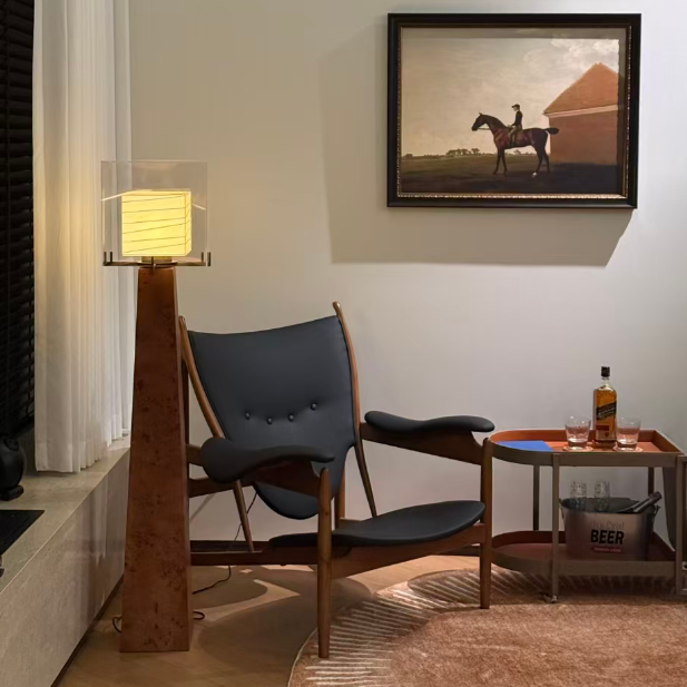 A framed art print depicting a silhouette of a rider on a horse in a field, hung on a beige wall in a modern living room setting next to a mid-century modern chair and a floor lamp.