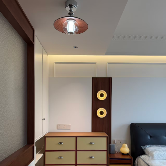 A modern bedroom interior featuring a mid-century style wooden dresser with cream drawers and dark wood trim, a matching nightstand, a dark leather headboard, and warm ambient lighting.