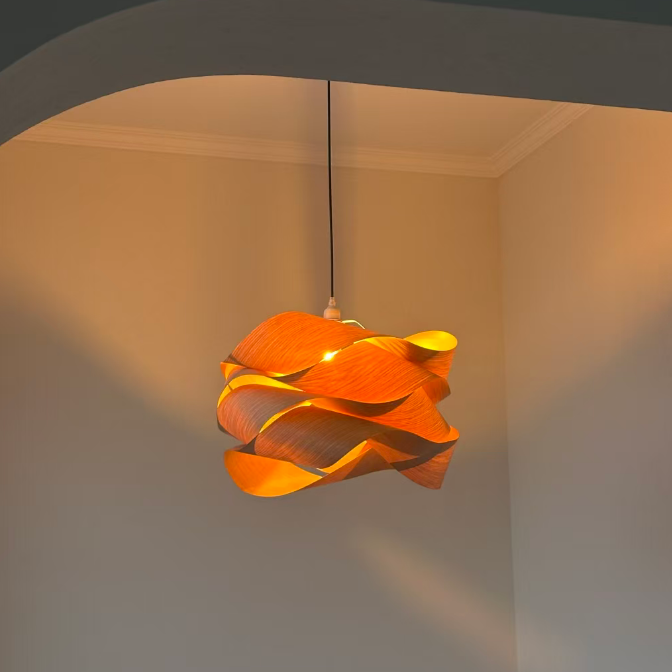 A modern spiral-shaped pendant light with a warm orange glow, hanging from a black cord in a minimalist room corner with beige walls.