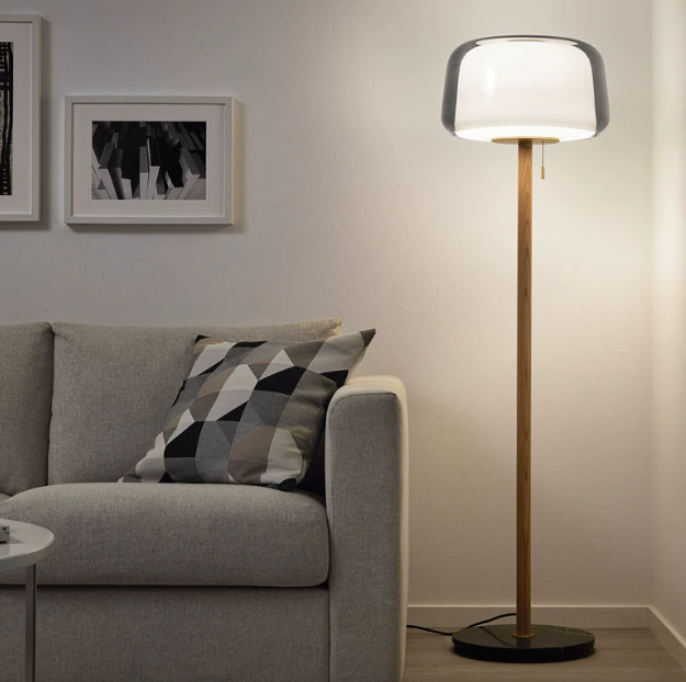 Smoked-glass floor lamp with wood stem and black base, shown beside a sofa