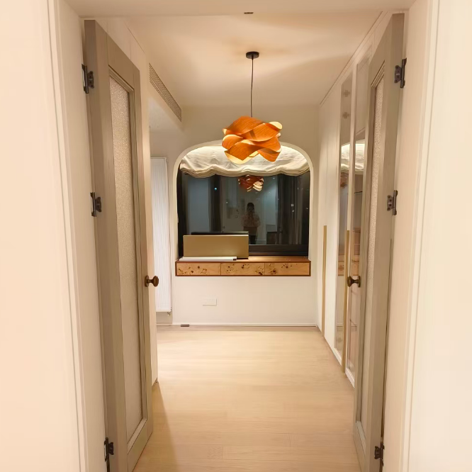 A modern home interior hallway with light wood floors, beige doors, and a distinctive orange flower-shaped pendant light hanging in the center above a console table.