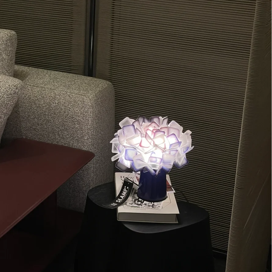 Geometric blossom table lamp with dark base and soft purple-white cube petal glow.