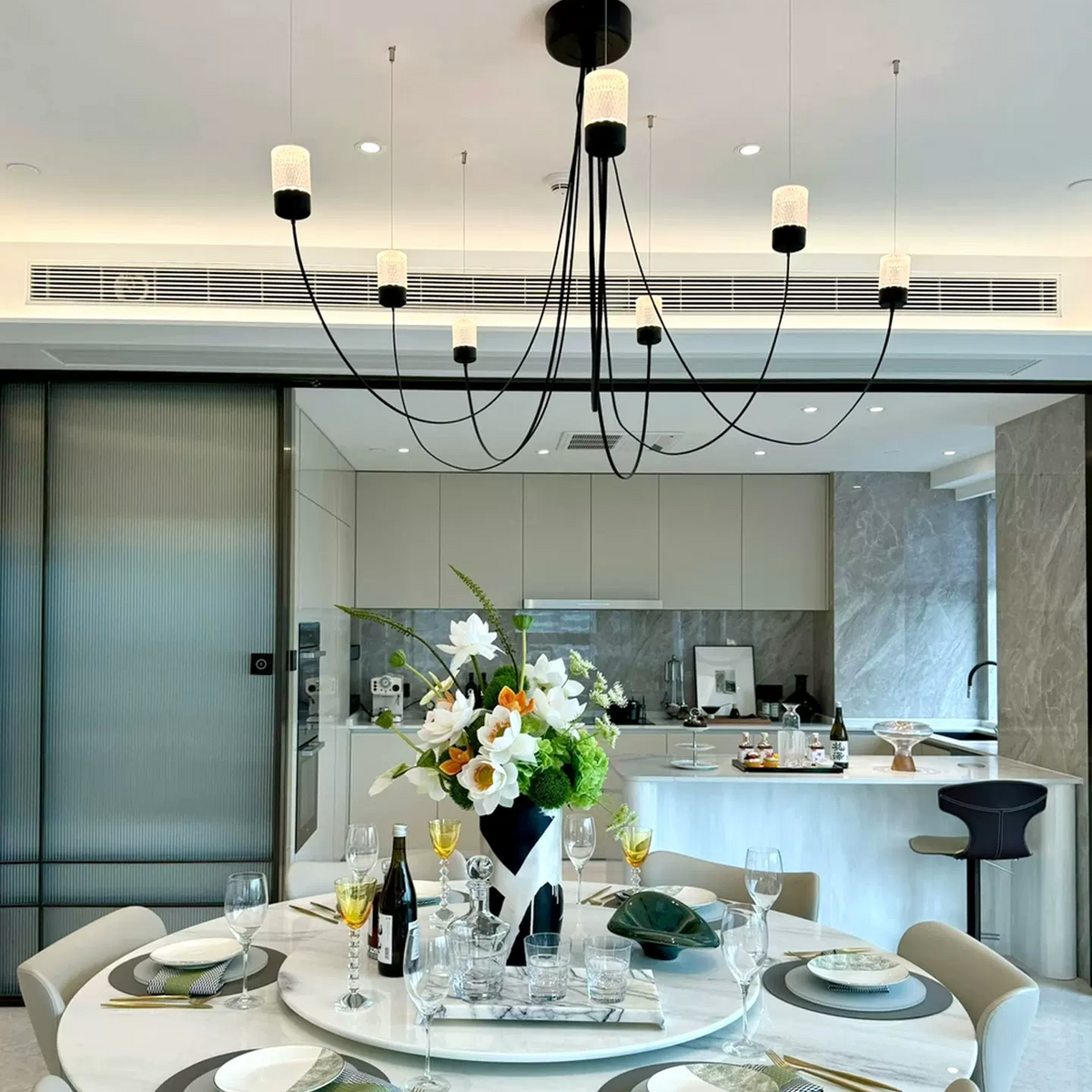Sculptural chandelier with black canopy, arcing cords, and multiple beige fabric cylinder shades