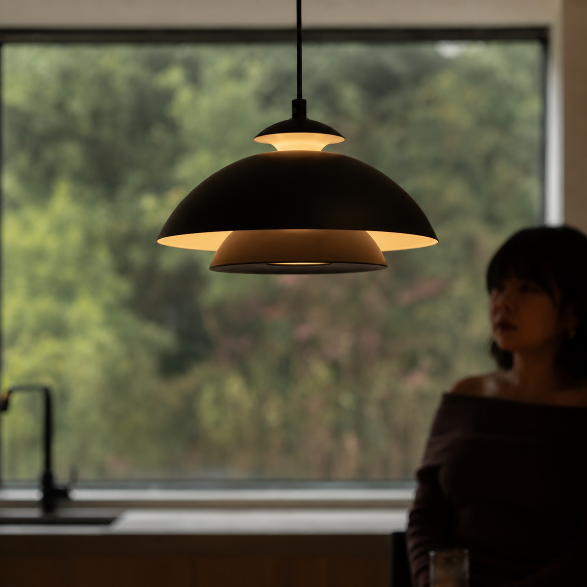 Close-up black dome pendant shade with warm glow, hanging from cord