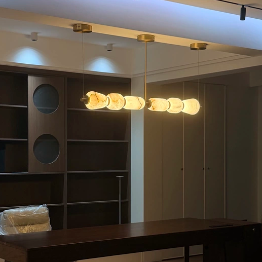 Linear chandelier with warm alabaster oval shades and brass accents, hanging from ceiling