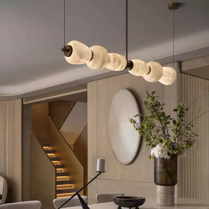 Gold linear chandelier with frosted circular shades near hallway wall and flowers
