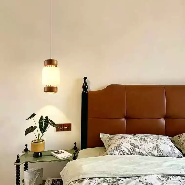 Mini pendant light over a bed: frosted glass cylinder shade with walnut trim and cord