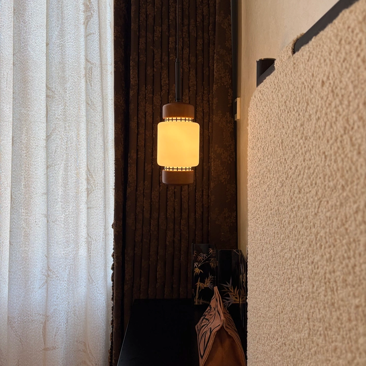 Lit walnut mini pendant light with frosted glass cylinder shade and dark ceiling cord