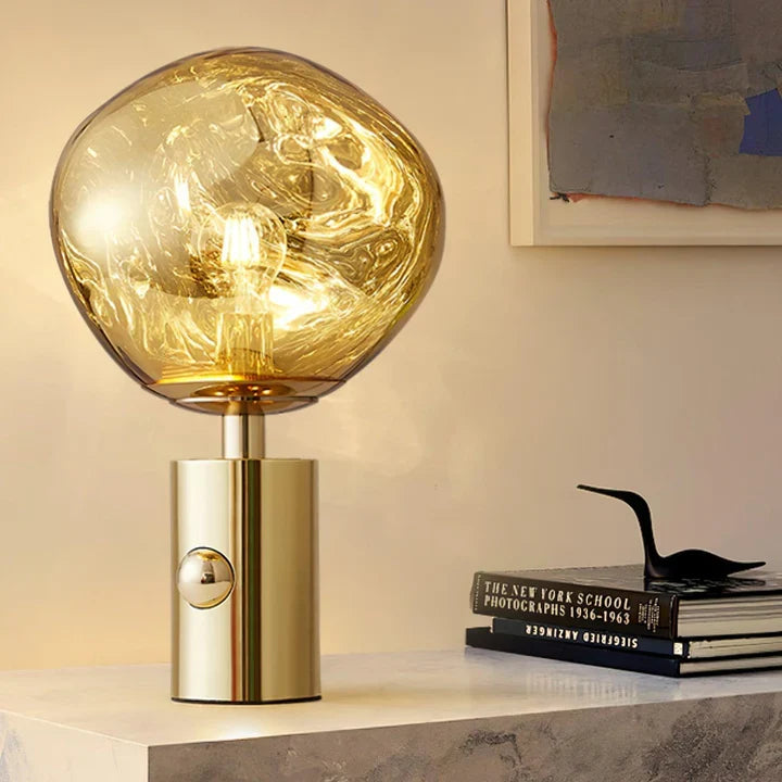 Gold table lamp with amber glass globe shade and glowing bulb