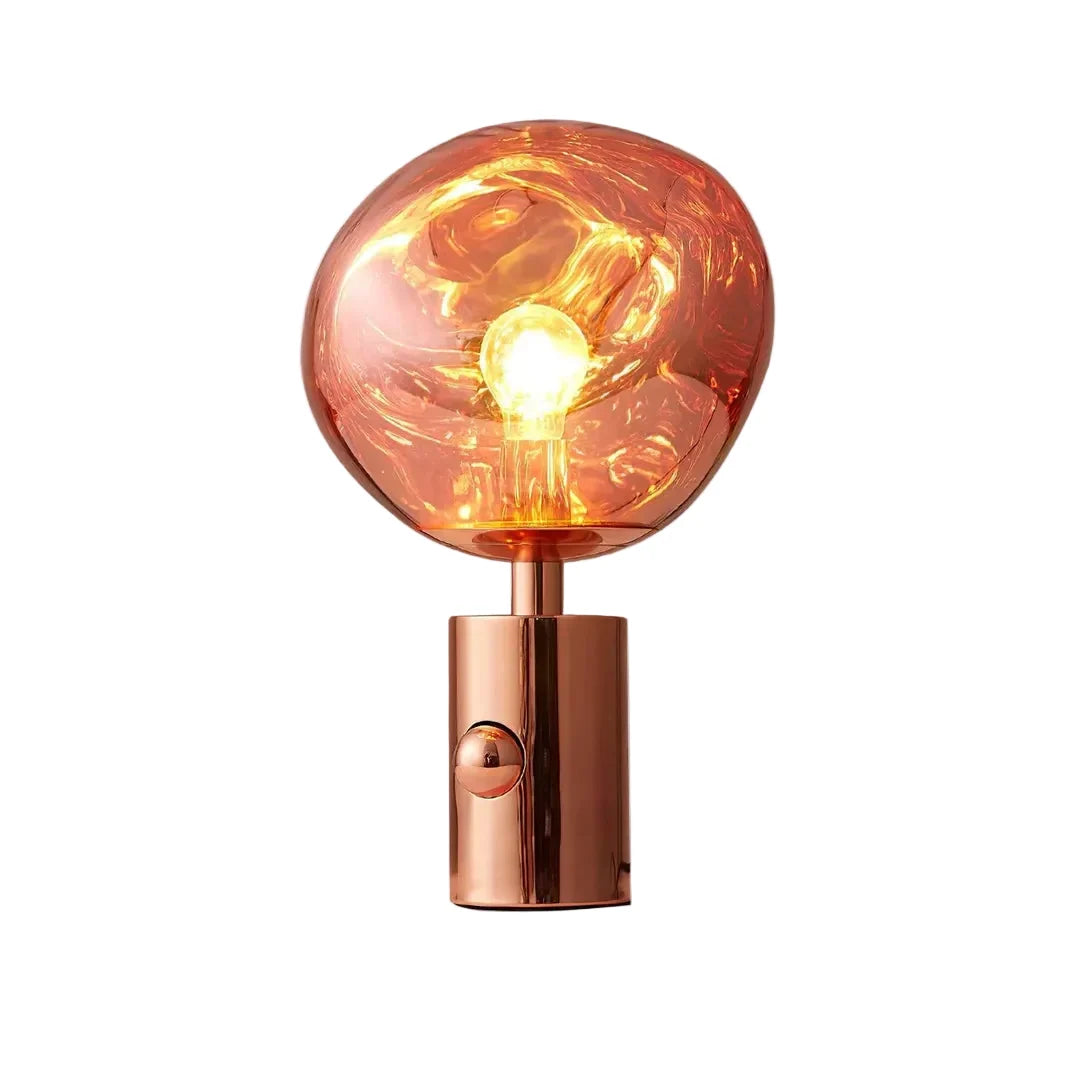 Rose gold table lamp with amber glass globe shade and glowing bulb inside