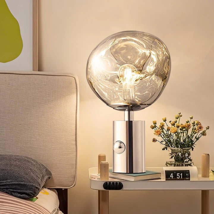 Silver table lamp with clear glass globe shade and glowing bulb on base
