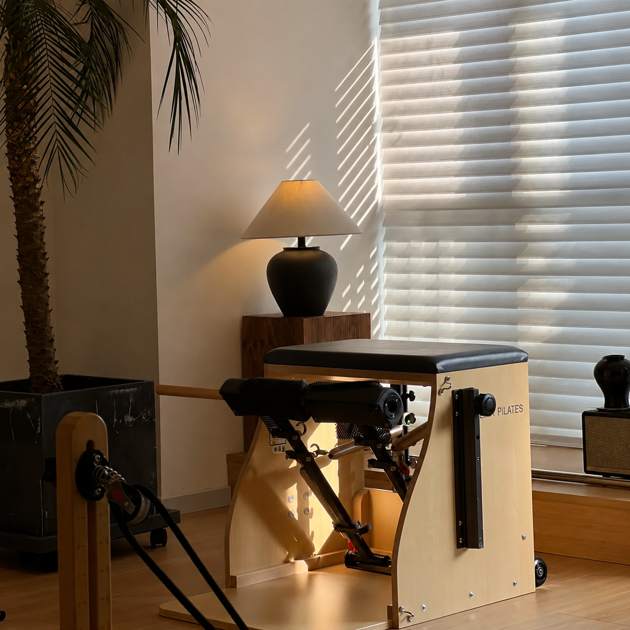 Ceramic table lamp with dark ceramic base and beige fabric drum shade beside blinds