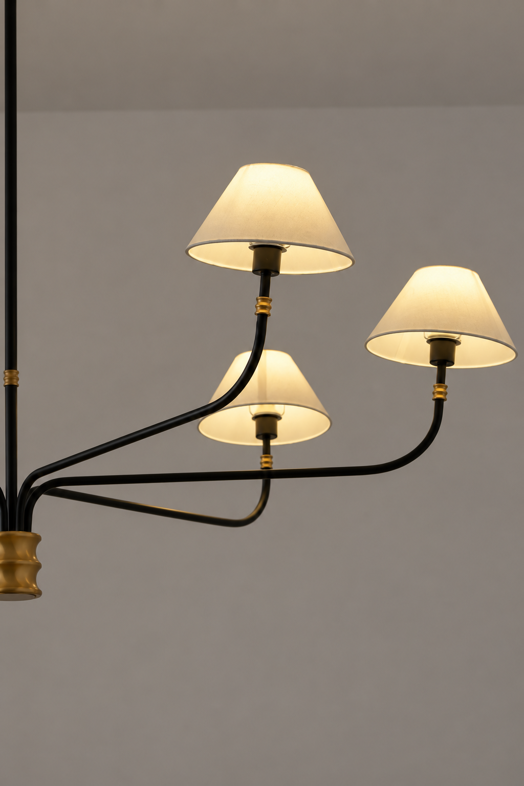 Close-up chandelier view: black arms with gold accents and cream fabric shades against wall.