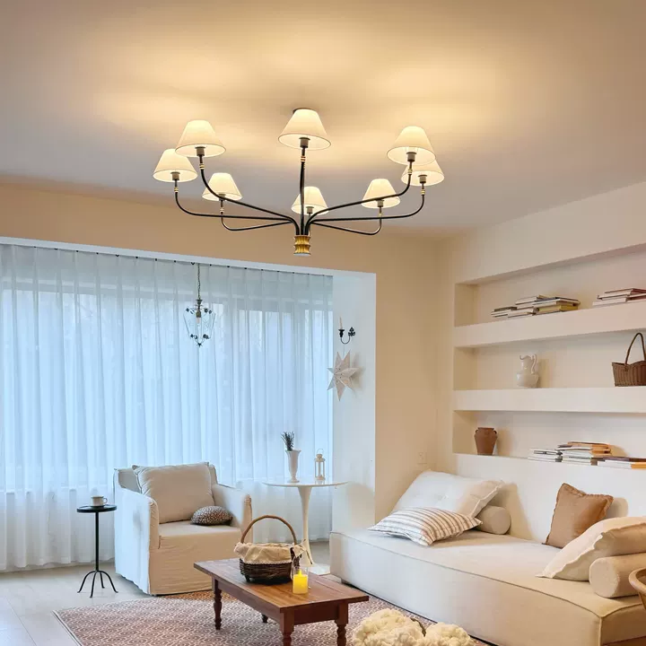 Black metal chandelier with cream fabric shades and gold detailing above a light living room.
