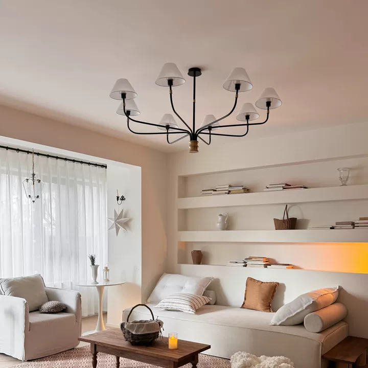 Black chandelier with cream fabric shades and gold finial, centered in a bright living room.